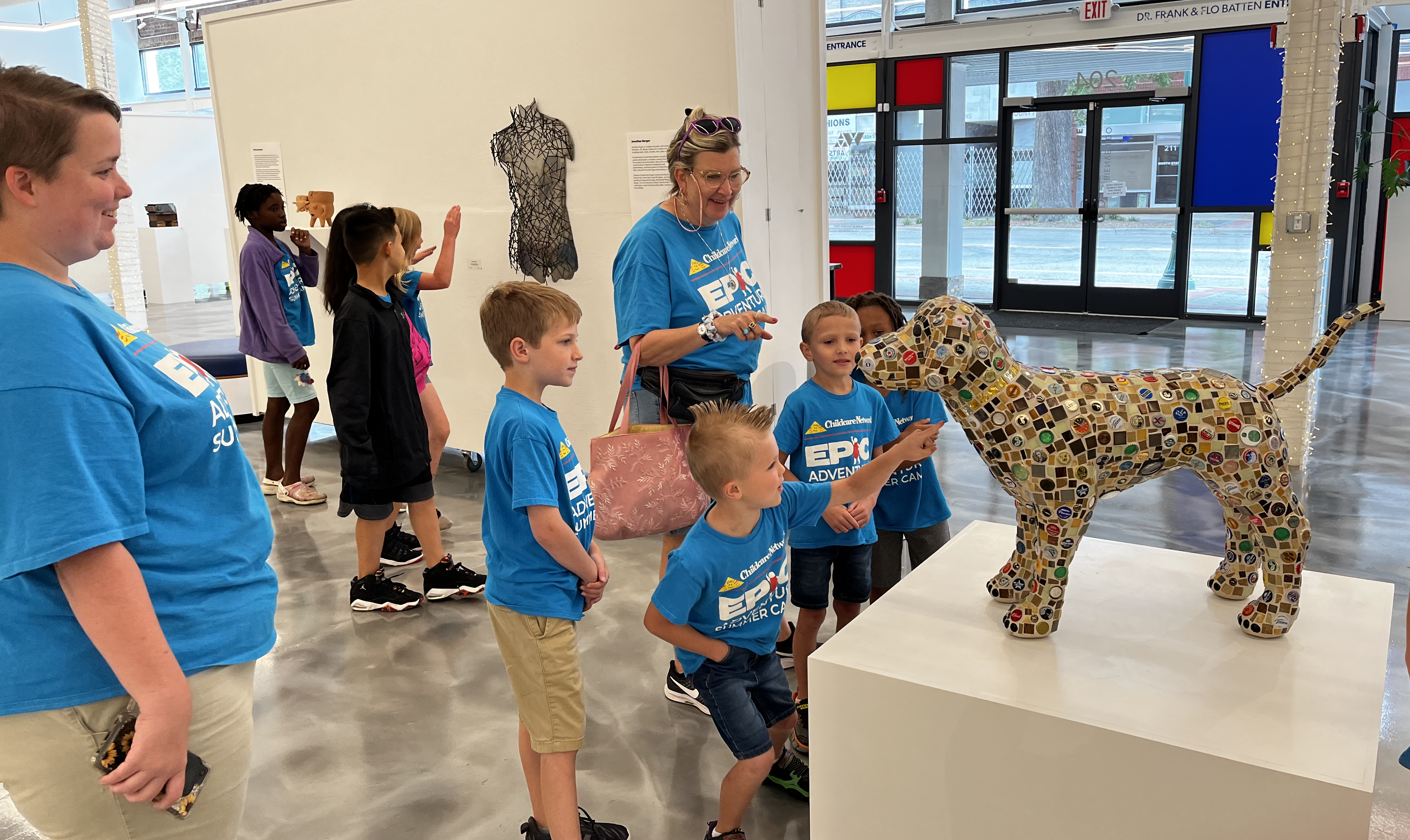 Young visitors in the gallery smiling as they look at a dog sculpture